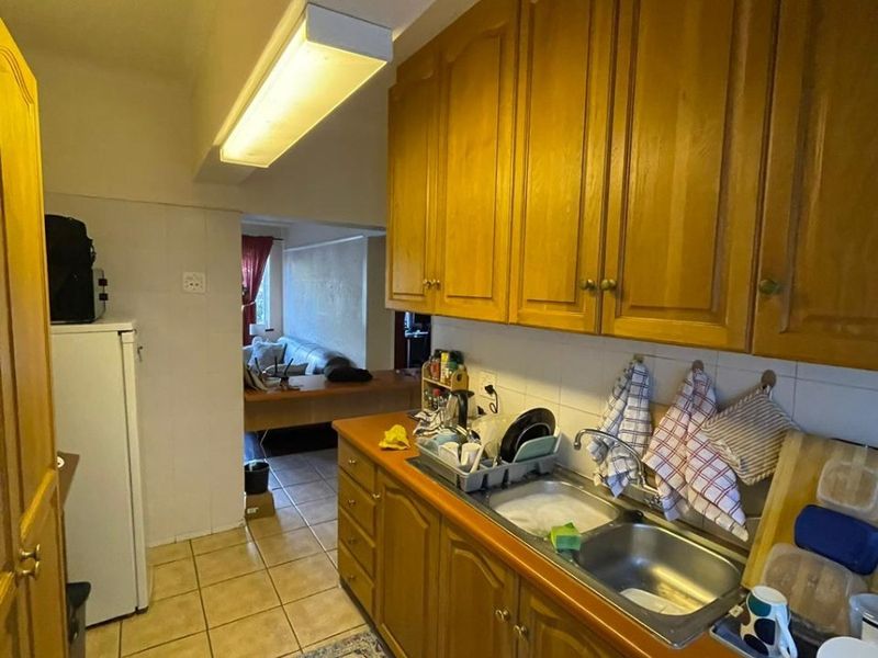 A functional kitchen featuring wooden cabinetry, a double stainless steel sink, and tiled flooring, offering a dated aesthetic ready for modernization.