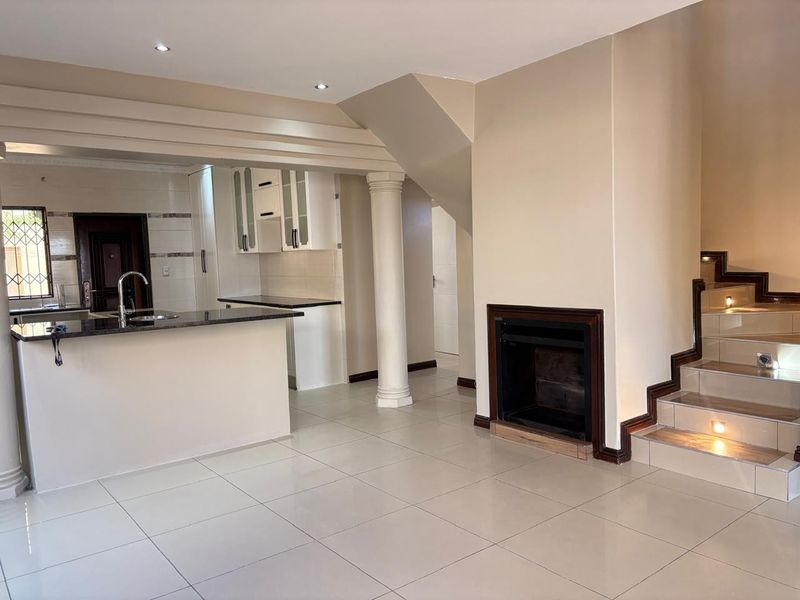 Spacious open-plan living area featuring a modern kitchen with granite countertops, a built-in fireplace, and a staircase with integrated lighting.