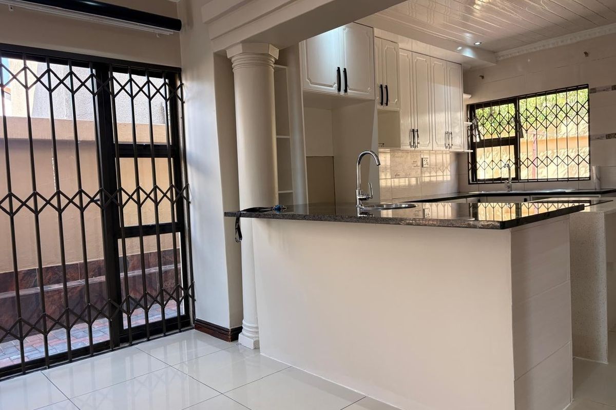 A clean, modern kitchen featuring granite countertops, white cabinetry, and tiled flooring, with a breakfast bar and direct access to an outdoor area.