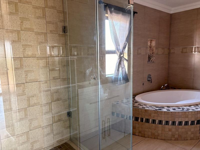 A spacious bathroom featuring a glass-enclosed shower and a built-in bathtub with decorative tiled surround and neutral wall tiling.