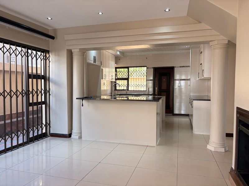 An open-plan living and kitchen area featuring tiled floors, decorative columns, a central kitchen island with granite countertops, and built-in cabinetry.