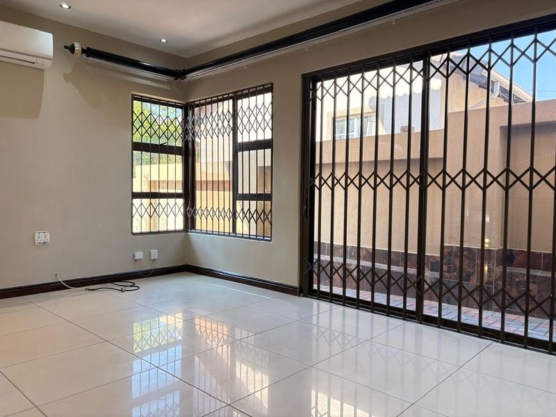 A bright, empty living area featuring polished tile floors, a split-system air conditioner, and large sliding doors with security gates leading to the exterior.
