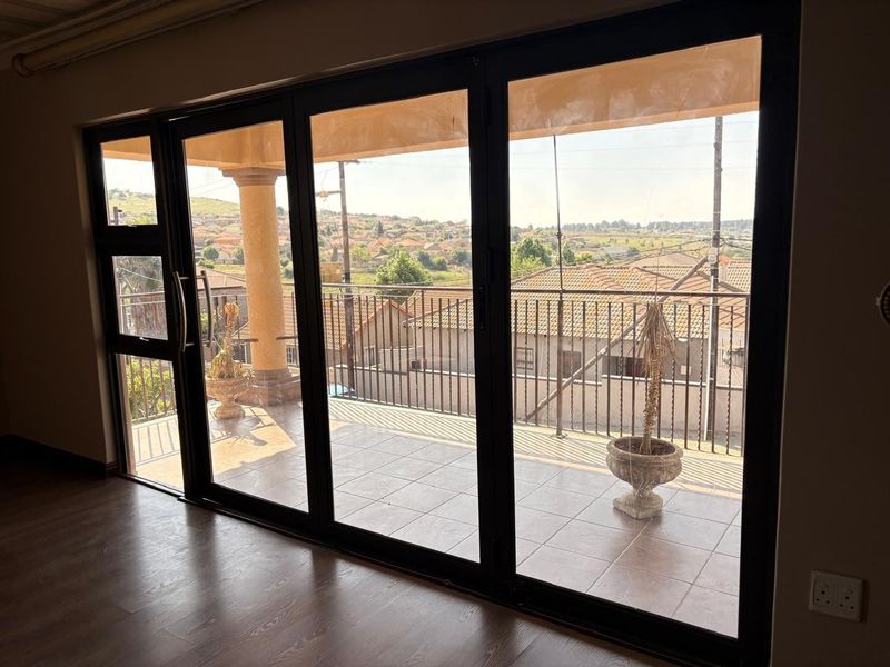 A covered balcony featuring tiled flooring, a metal balustrade, and large sliding glass doors, offering an elevated view of the surrounding neighborhood.