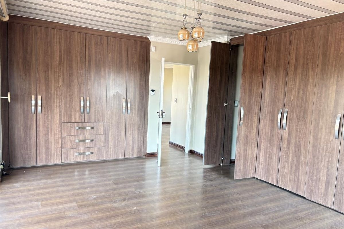Spacious bedroom featuring extensive built-in wooden cabinetry, laminate flooring, and a modern ceiling light fixture.