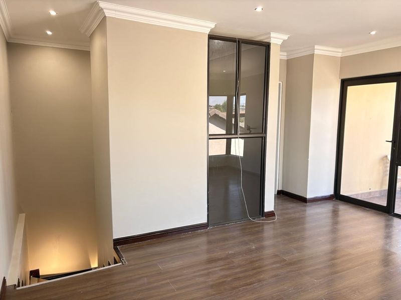 An open-plan living area featuring laminate flooring, recessed lighting, crown molding, and access to an outdoor balcony through a sliding glass door.