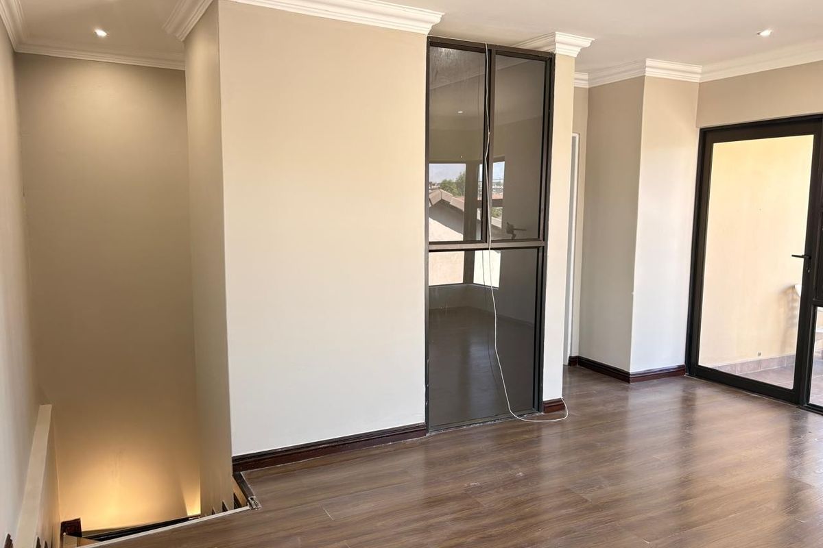 An open-plan living area featuring laminate flooring, recessed lighting, crown molding, and access to an outdoor balcony through a sliding glass door.