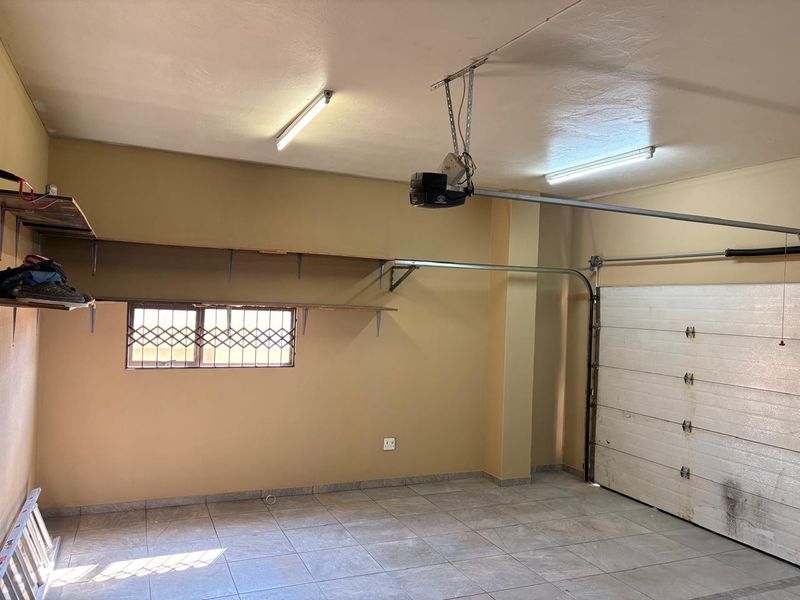 A functional double garage featuring tiled flooring, built-in shelving, security bars on the window, and an automated garage door motor.