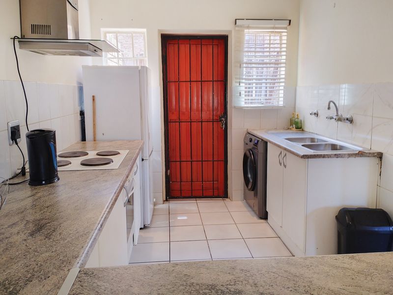 A functional kitchen featuring laminate countertops, built-in cabinetry, an electric hob with extractor fan, and a double sink with tiled backsplash.