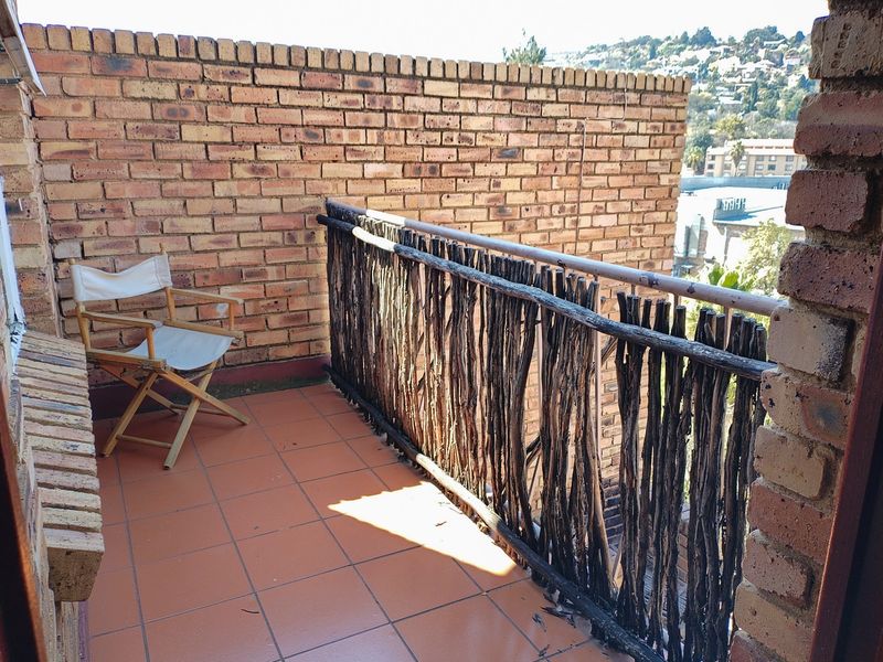 A private balcony featuring a brick wall, tiled flooring, and a rustic timber balustrade with views of the surrounding area.