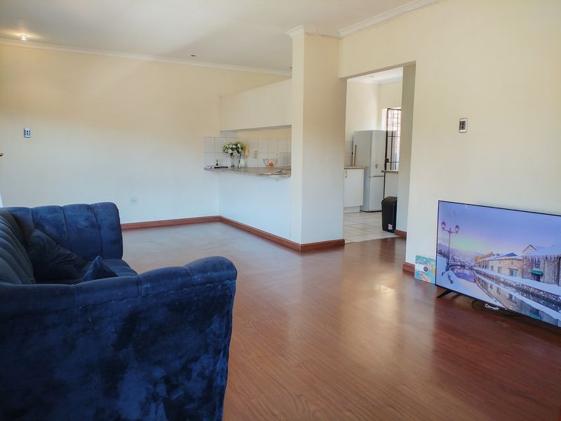 Open plan living area featuring laminate flooring and a kitchen breakfast bar with tiled splashback, offering a functional layout for modern apartment living.