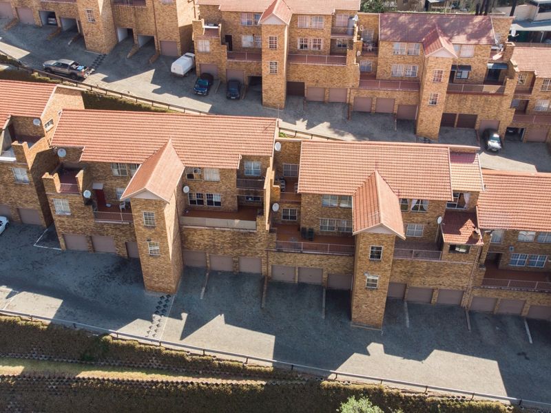 Aerial view of a multi-unit apartment complex featuring face-brick construction, tiled roofing, integrated garages, and private balconies.