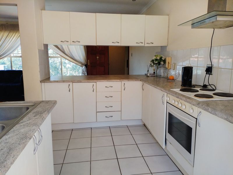 A functional kitchen featuring white cabinetry, laminate countertops, tiled flooring, and built-in appliances including an oven, hob, and extractor fan.