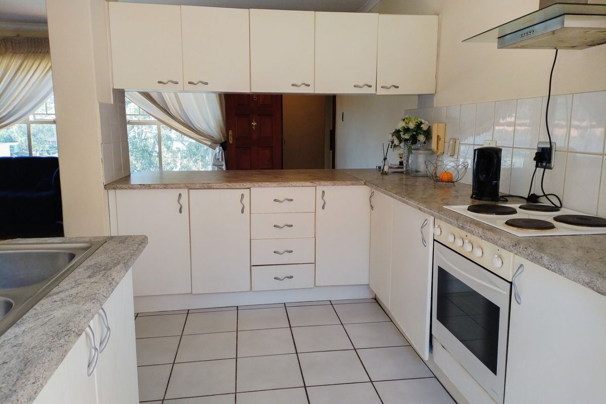 A functional kitchen featuring white cabinetry, laminate countertops, tiled flooring, and built-in appliances including an oven, hob, and extractor fan.