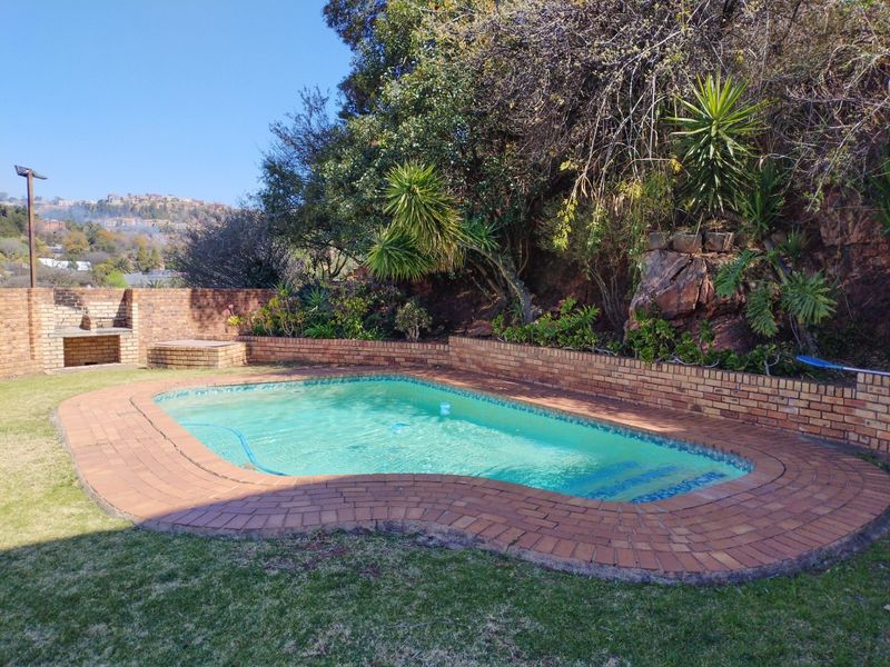 Outdoor pool area featuring a swimming pool with brick paving, a built-in braai, and a brick boundary wall set against a natural rock backdrop.