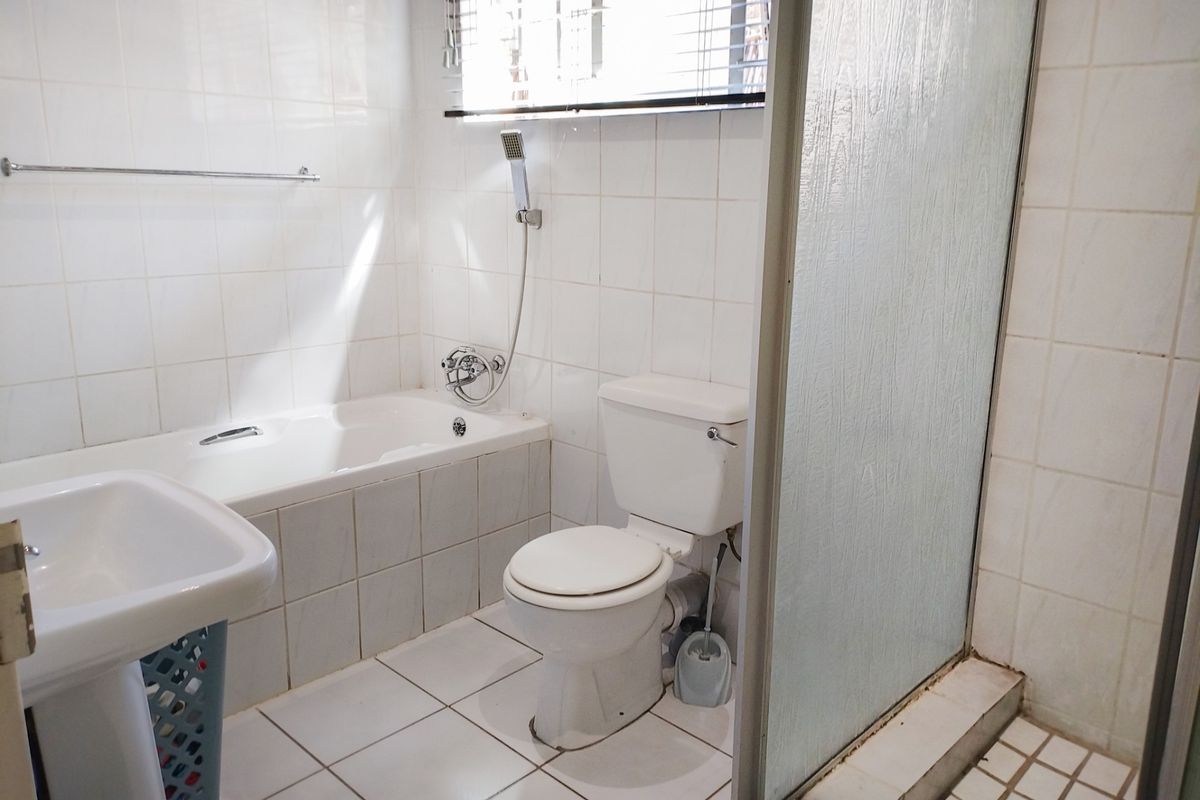 A functional bathroom featuring a bathtub, separate shower enclosure, pedestal basin, and toilet with white tiled finishes throughout.