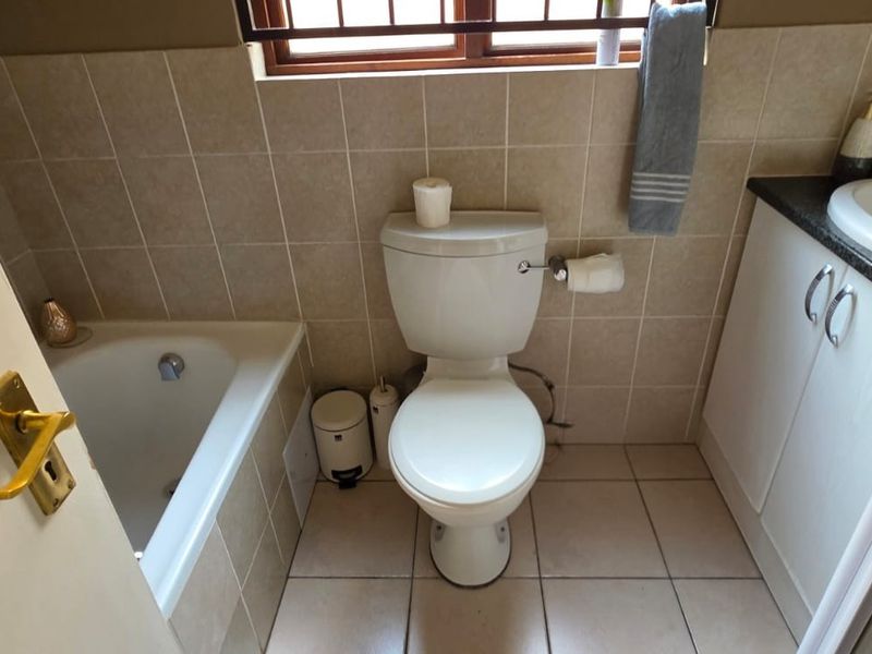 A functional bathroom featuring a built-in bathtub, a vanity with a drop-in basin, and neutral ceramic tiling throughout.
