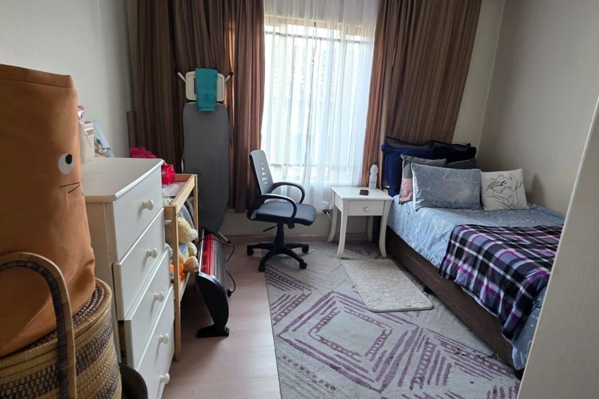 A functional bedroom featuring laminate flooring and large window with curtain tracks, providing natural light to the space.