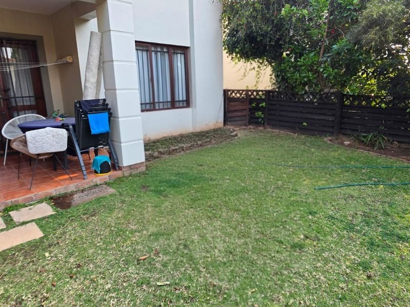 Rear view of the apartment featuring a tiled patio area, sliding glass doors, and a private garden with a timber fence boundary.
