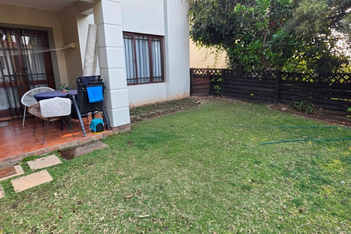 Rear view of the apartment featuring a tiled patio area, sliding glass doors, and a private garden with a timber fence boundary.