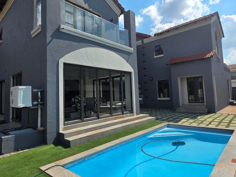 Rear view of a modern two-story house featuring a swimming pool, paved patio area, and a balcony with glass railings.