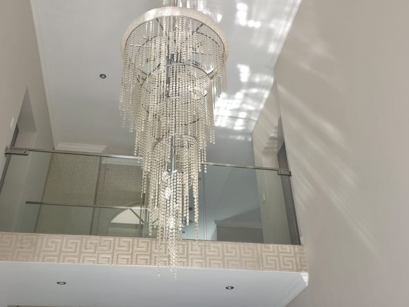 A bright double-volume entrance hallway featuring a modern glass balustrade and an elegant tiered crystal chandelier.