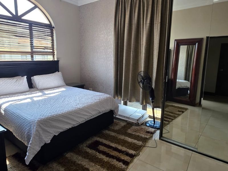 A bedroom featuring tiled flooring, an arched window with blinds, and a large built-in mirrored wardrobe.