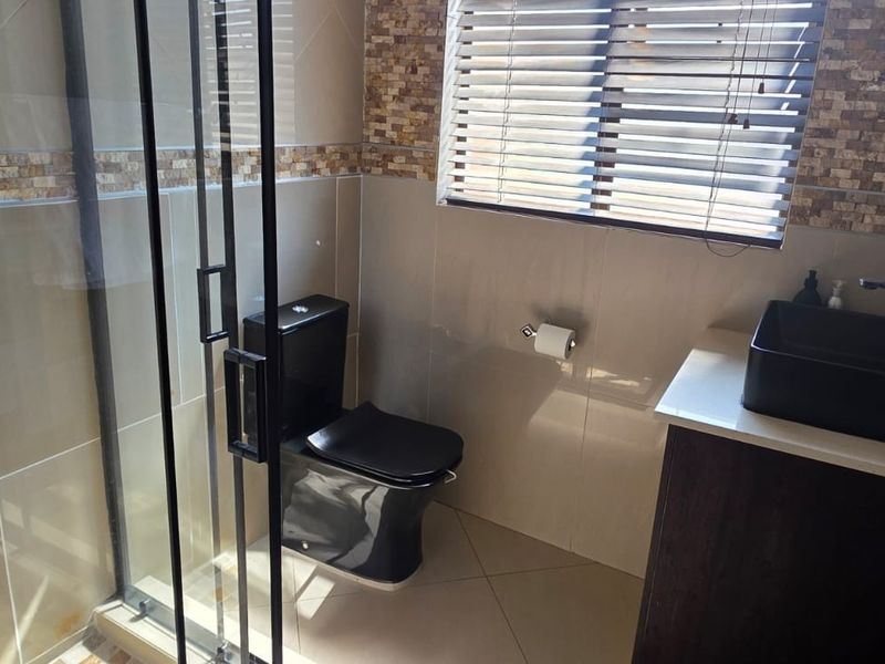 Modern bathroom featuring a glass shower enclosure, black toilet, vessel sink with vanity, and decorative stone tile accents.