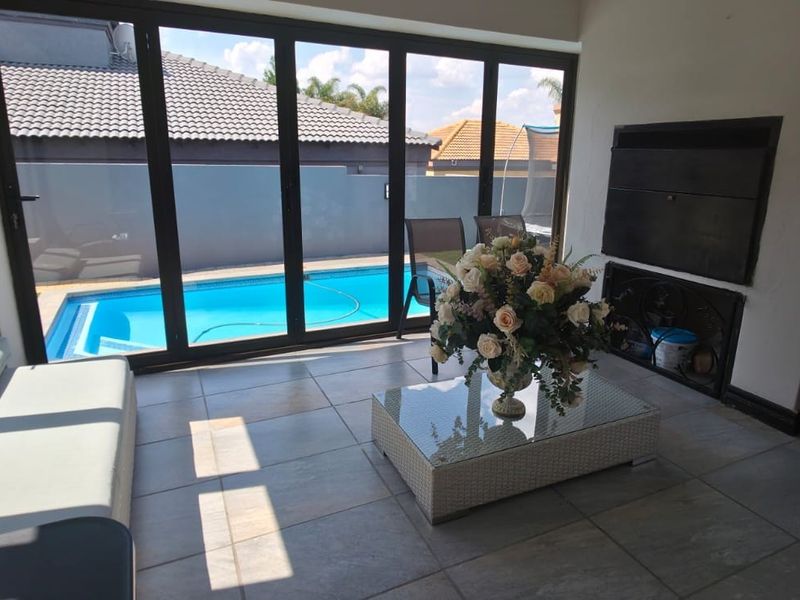 Covered patio area featuring tiled flooring, a built-in braai, and large aluminium stack doors opening directly onto the swimming pool area.