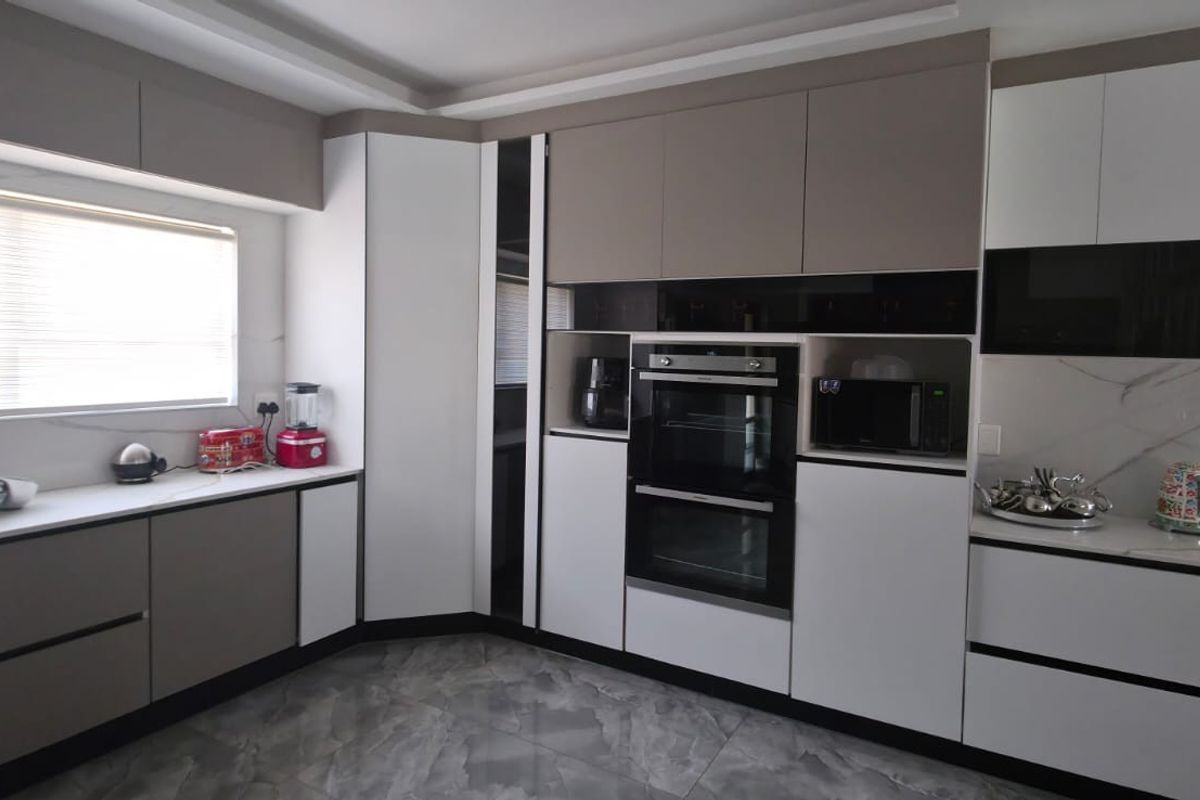 Modern kitchen featuring sleek two-tone cabinetry, integrated double oven, marble-look splashbacks, and high-quality stone countertops with ample storage space.
