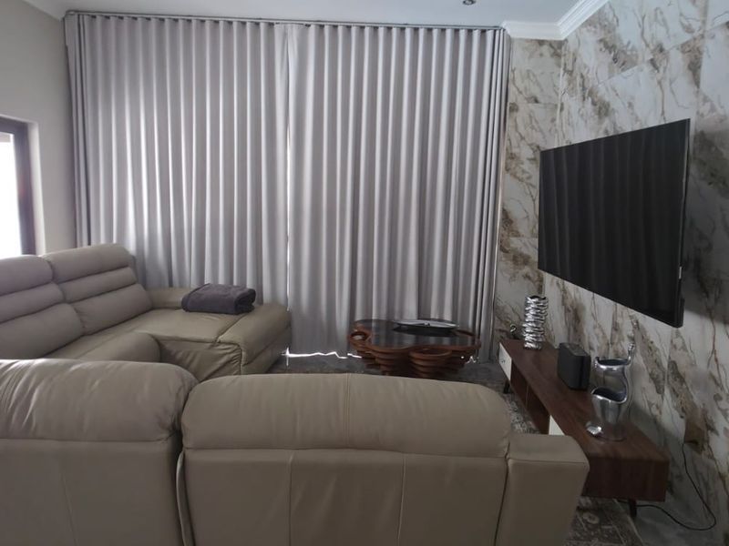 A modern living room featuring a striking marble-effect feature wall, recessed ceiling lighting, and large windows with floor-to-ceiling curtains.