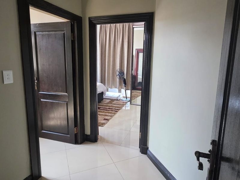 A clean, well-maintained hallway featuring neutral tiled flooring and dark wood door frames, providing access to adjacent rooms.