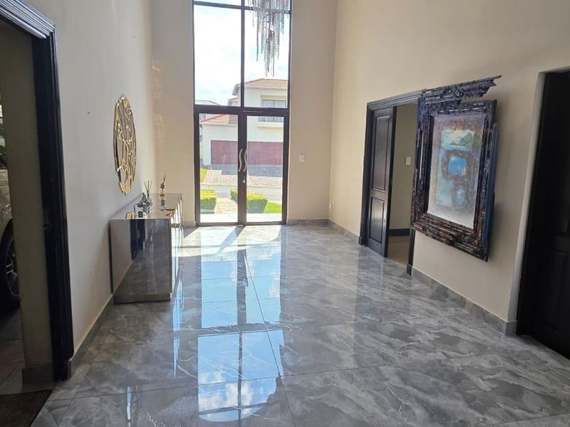 Spacious double-volume entrance hall featuring high ceilings, full-height glass doors, and polished marble-look floor tiles, creating a bright and welcoming atmosphere.