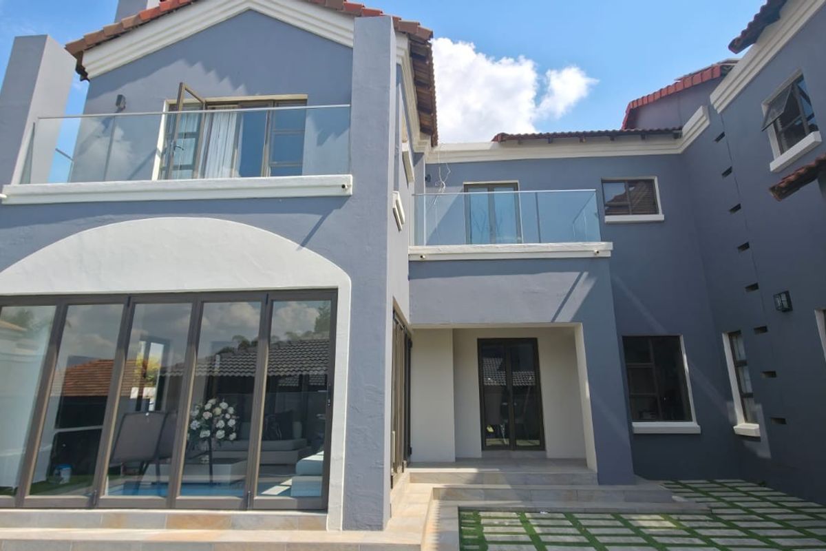 Rear elevation of a modern double-storey house featuring glass balustrades, large aluminium sliding doors, and a paved patio area.