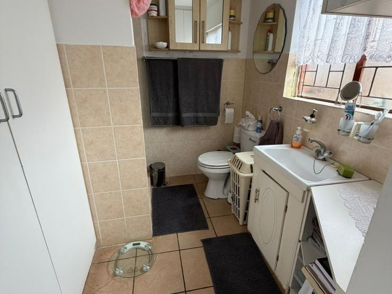 A functional bathroom featuring a vanity cabinet with basin, toilet, wall-mounted storage, and tiled finishes throughout.