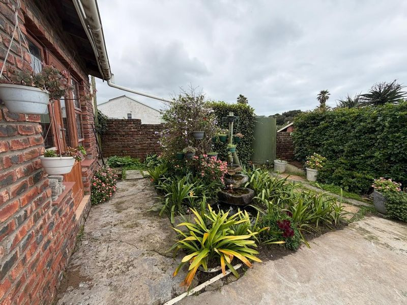 A rear garden area featuring a brick facade, stone paving, a water feature, and a water tank, enclosed by a brick boundary wall.