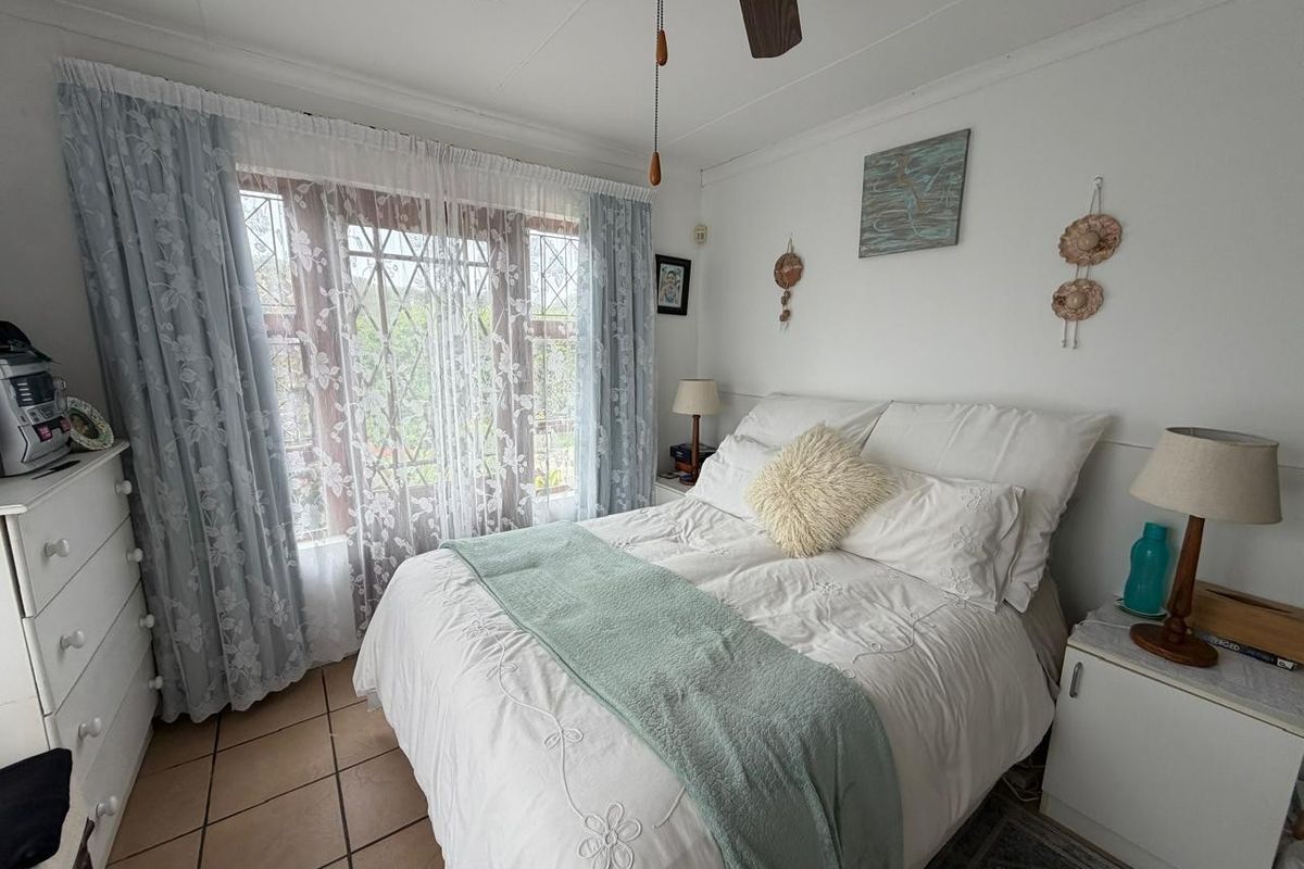A cozy bedroom featuring tiled flooring, a ceiling fan, and a window fitted with security bars, offering a functional and comfortable living space.