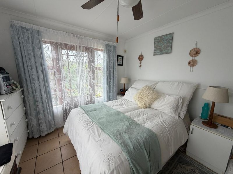 A cozy bedroom featuring tiled flooring, a ceiling fan, and a window fitted with security bars, offering a functional and comfortable living space.