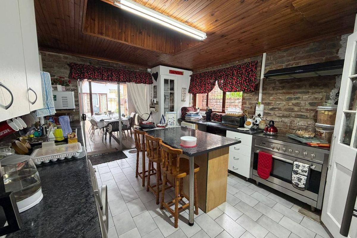 A rustic kitchen featuring exposed brick walls, timber ceiling, granite countertops, and a large gas stove, with direct access to an outdoor patio area.
