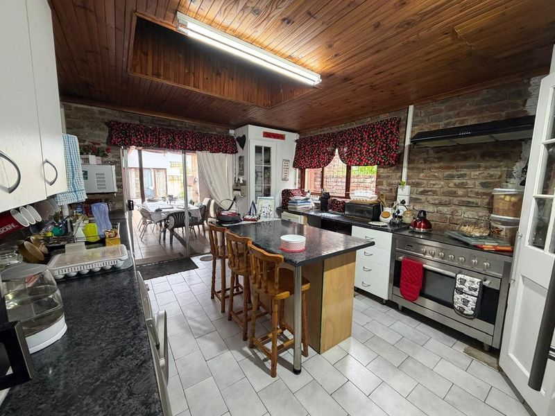 A rustic kitchen featuring exposed brick walls, timber ceiling, granite countertops, and a large gas stove, with direct access to an outdoor patio area.