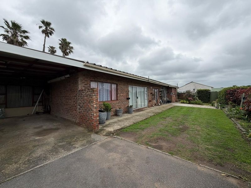 Rear view of a brick house featuring a carport, sliding glass doors, and a private garden area with a concrete pathway.