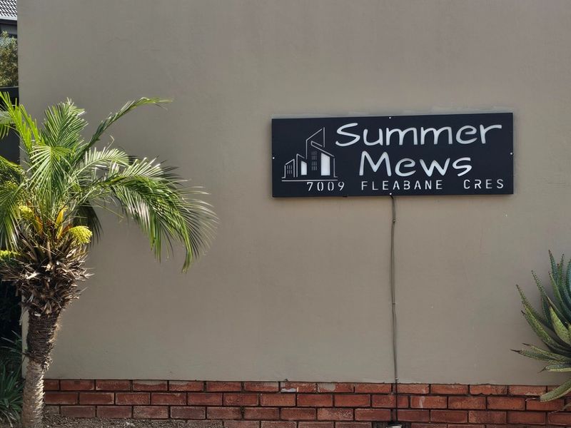 Exterior view of the Summer Mews townhouse complex entrance signage featuring a plastered wall with brick base and landscaped greenery.