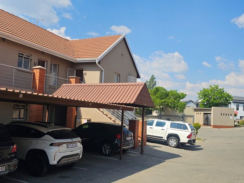Exterior view of a townhouse complex featuring a paved driveway, covered carports, and multi-story residential units with tiled roofing.