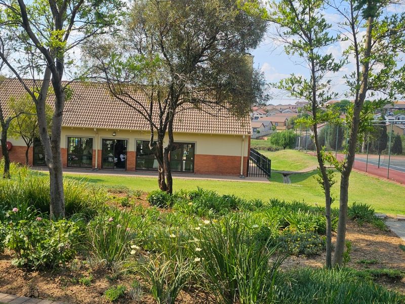 A view of the rear exterior of the townhouse complex, featuring a landscaped garden, paved walkway, and access to a communal tennis court.