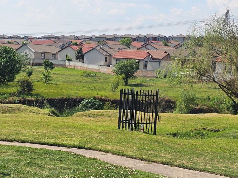 A wide-angle view of a residential estate featuring a paved walkway, open green space, and surrounding townhouse properties.