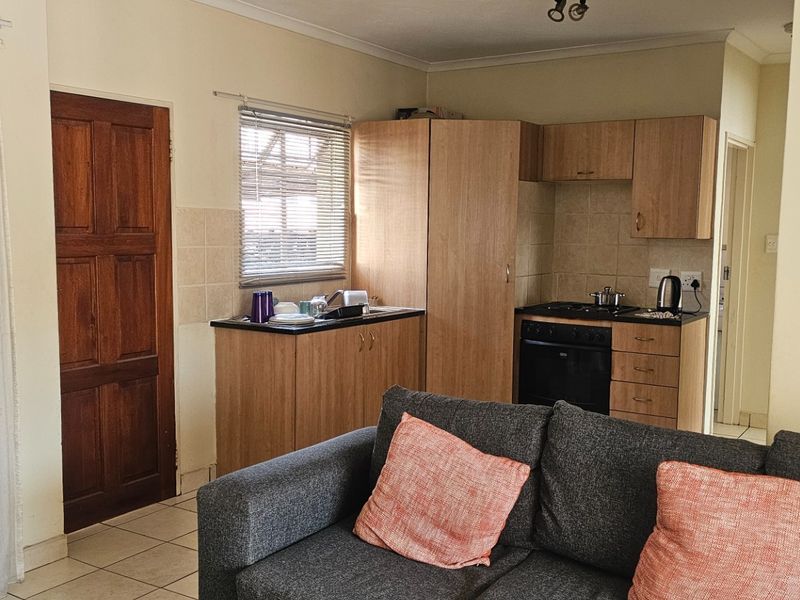 Open plan living area featuring a compact kitchen with built-in cabinetry, gas hob, and oven, finished with tiled flooring and neutral wall tones.
