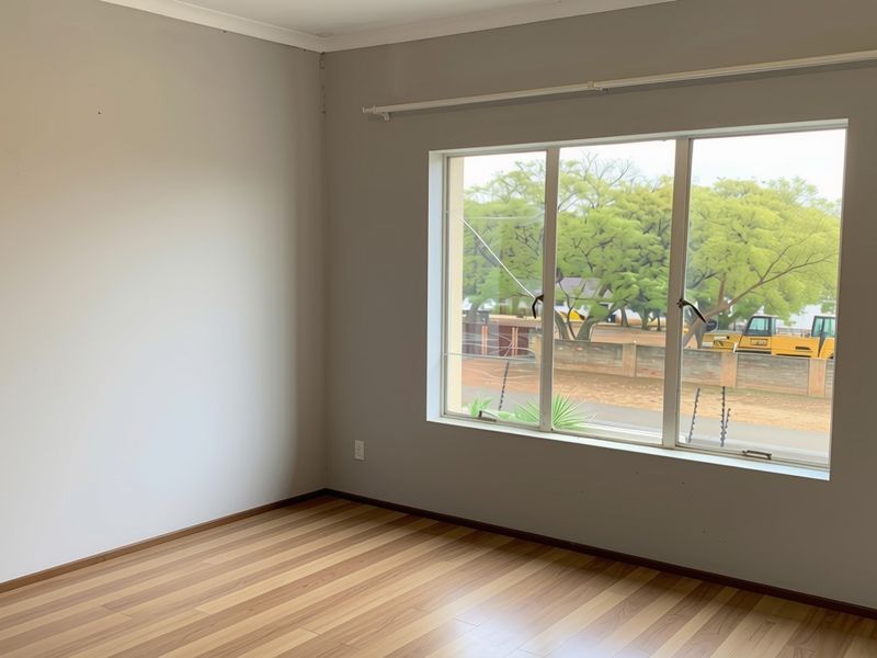 An empty bedroom featuring laminate flooring and a large window with a cracked pane, offering a view of the street.