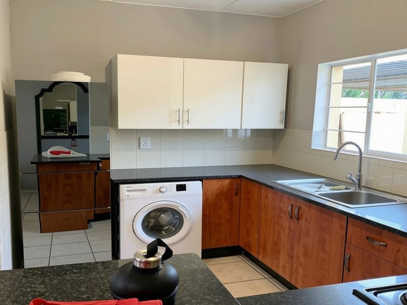 Functional kitchen featuring wood-finish lower cabinetry, white upper cabinets, dark laminate countertops, and a stainless steel sink with a tiled backsplash.