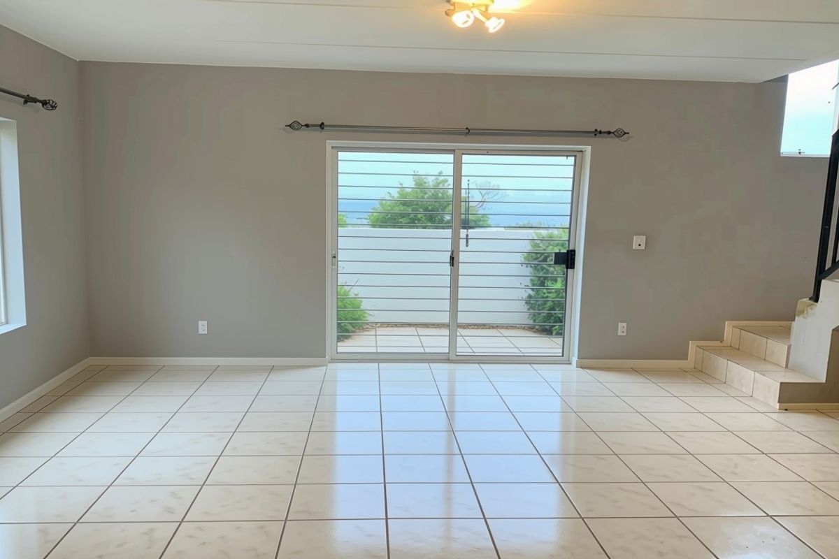 Spacious, light-filled living area featuring neutral tiled flooring, a sliding door with security gate, and an internal staircase.