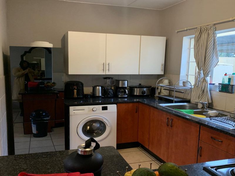A functional kitchen featuring wood-finish cabinetry, dark granite countertops, tiled flooring, and a built-in washing machine, offering a practical layout for daily use.