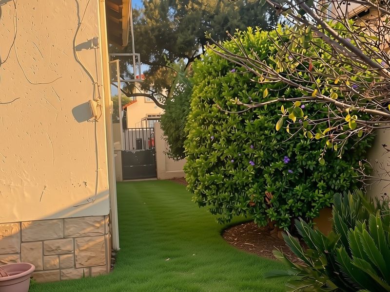 A well-maintained rear garden area featuring a manicured lawn, mature shrubbery, and a secure metal gate access point.